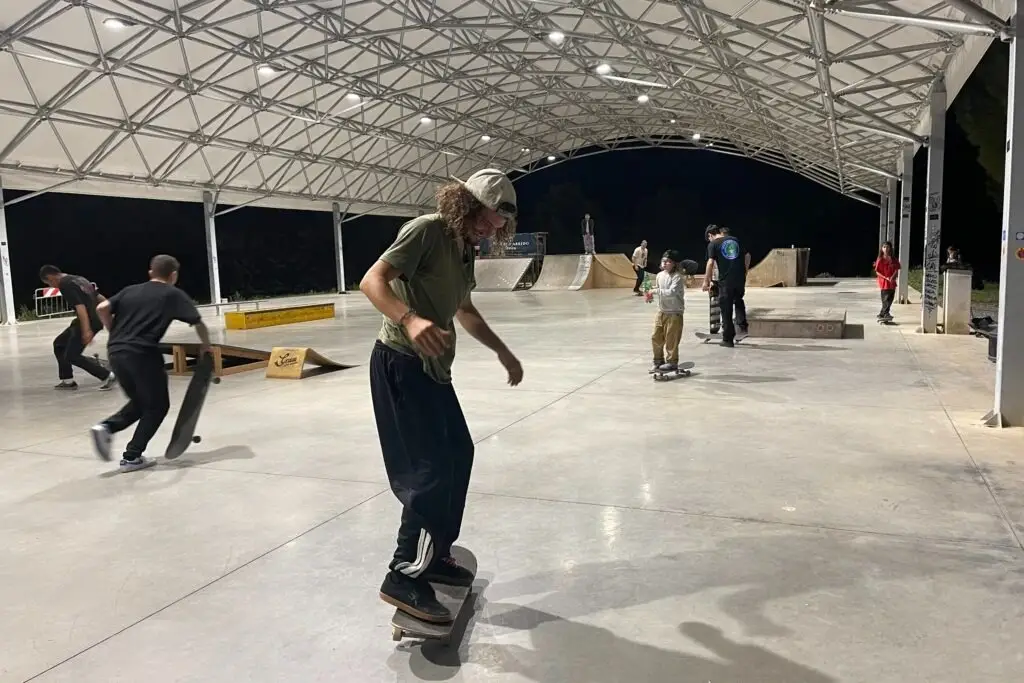 Skatepark in uso sotto una copertura ad arco a falde, con struttura reticolare in acciaio a vista