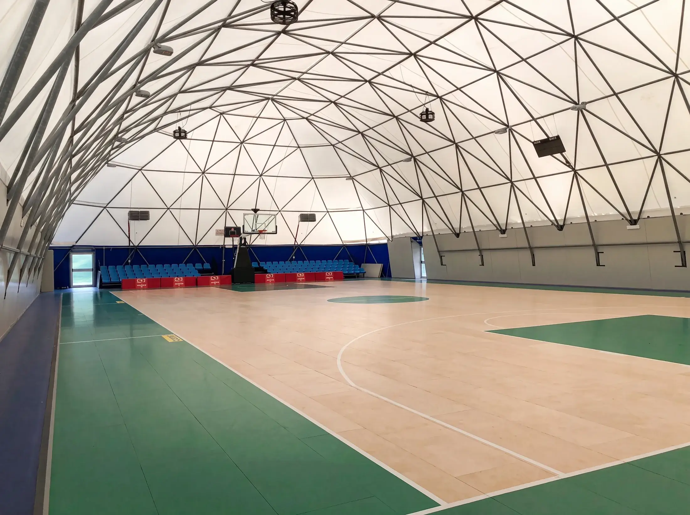 Interno di una palestra da basket coperta da una struttura geodetica, con parquet, tribuna e canestro